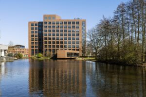 Kantoorgebouw aan de Prof. W.H. Keesomlaan met spiegeling in het water en omliggende bomen.